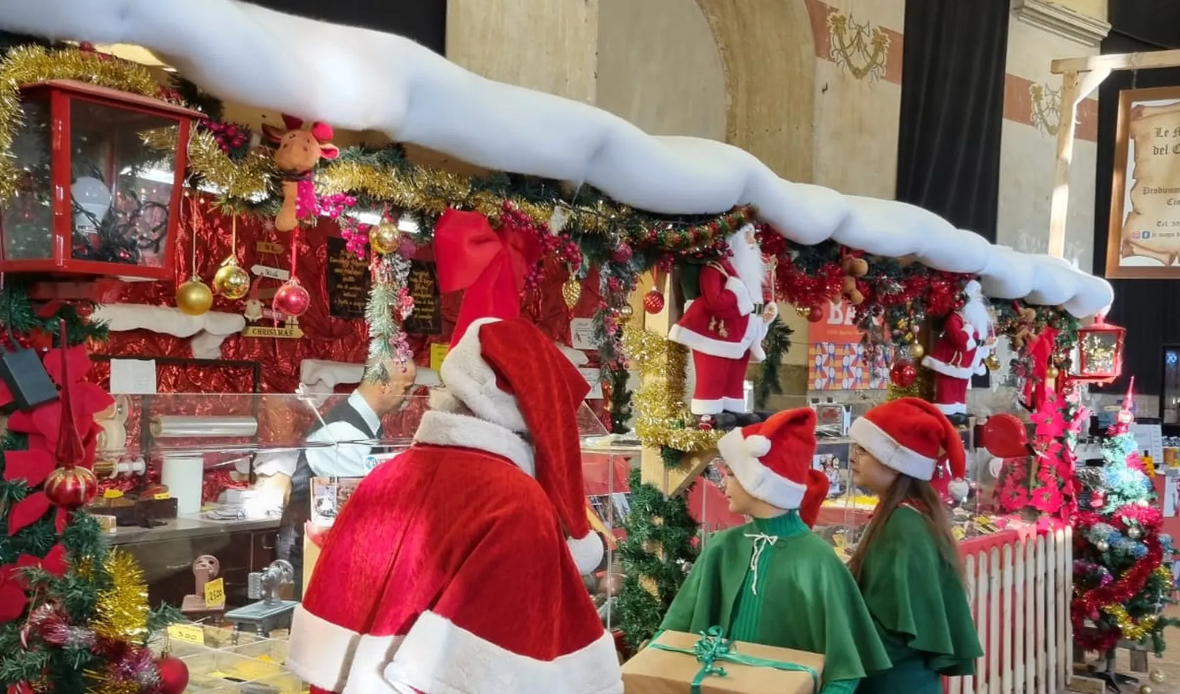 Babbo Natale con gli elfi vicino a una bancarella del mercatino