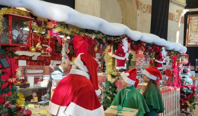 Babbo Natale con gli elfi vicino a una bancarella del mercatino